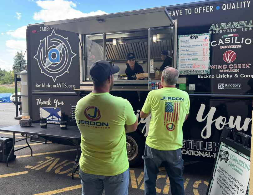 Two people wearing shirts with the Jerdon Construction logos on them ordering from a food truck